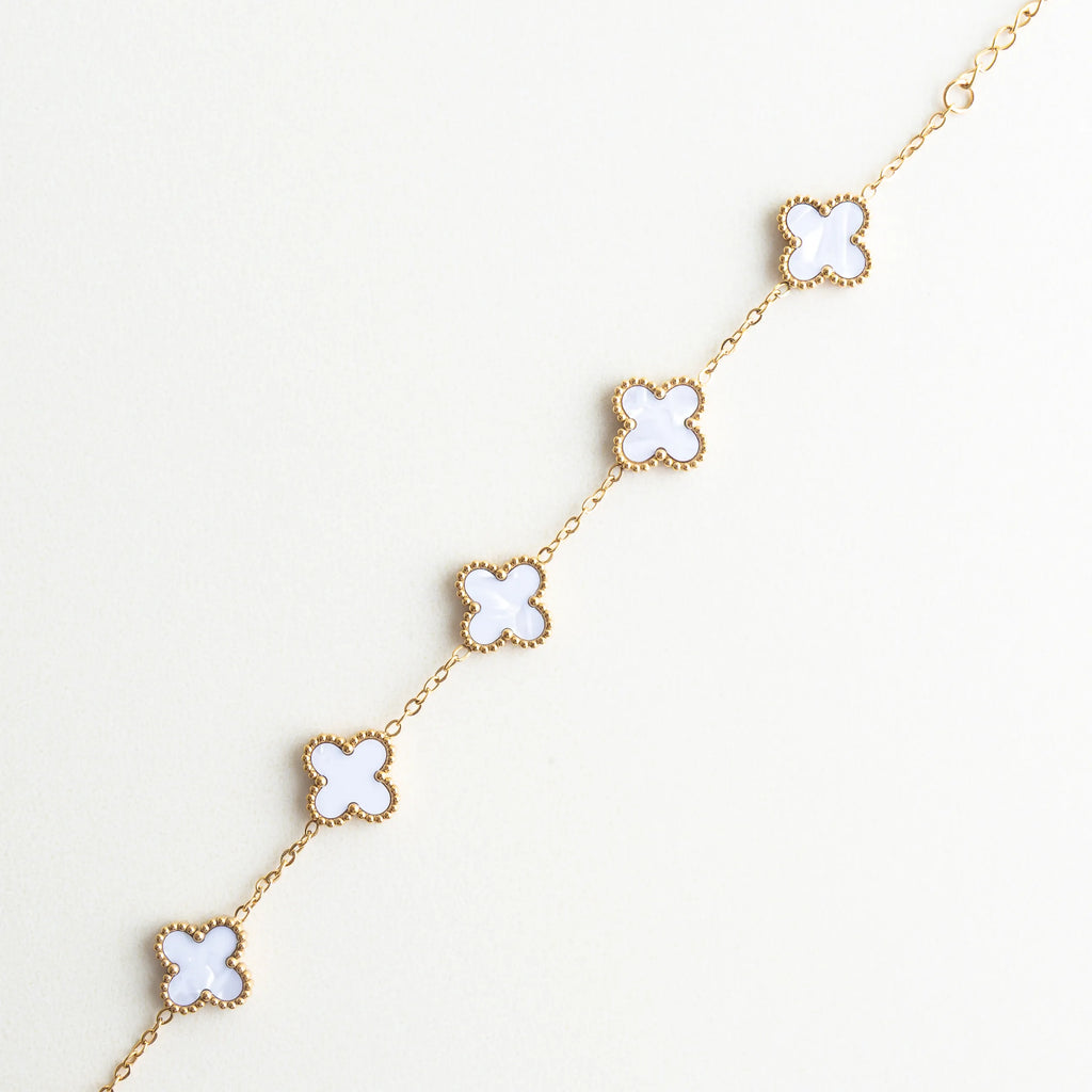 Detalle de dijes de trébol blanco en pulsera dorada, Acercamiento a tréboles de nácar con acabado brillante, Detalle de piedras de nácar en forma de trébol, Pulsera con dijes de trébol mostrando textura y brillo, Diseño de trébol blanco con acabado en oro 18K