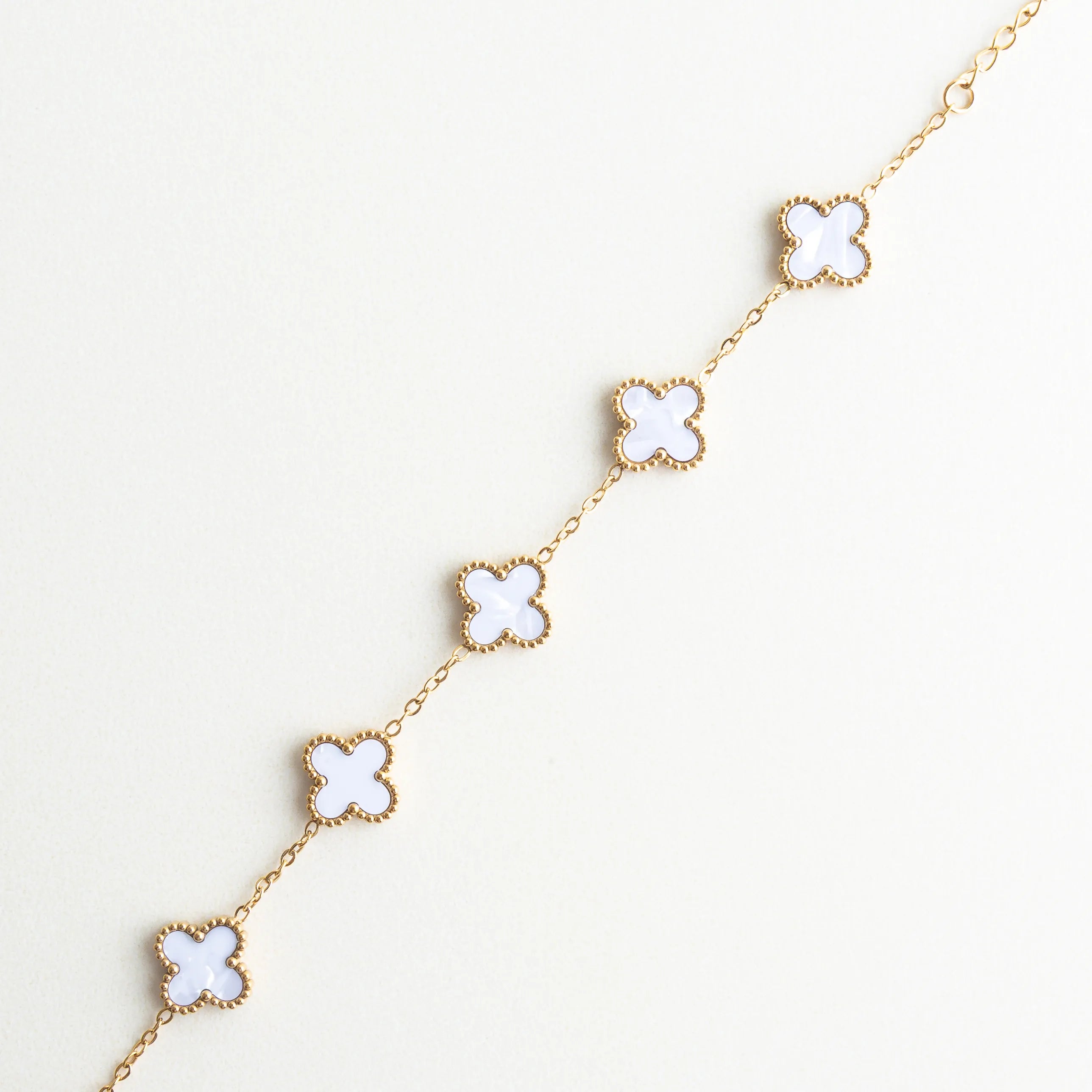 Detalle de dijes de trébol blanco en pulsera dorada, Acercamiento a tréboles de nácar con acabado brillante, Detalle de piedras de nácar en forma de trébol, Pulsera con dijes de trébol mostrando textura y brillo, Diseño de trébol blanco con acabado en oro 18K