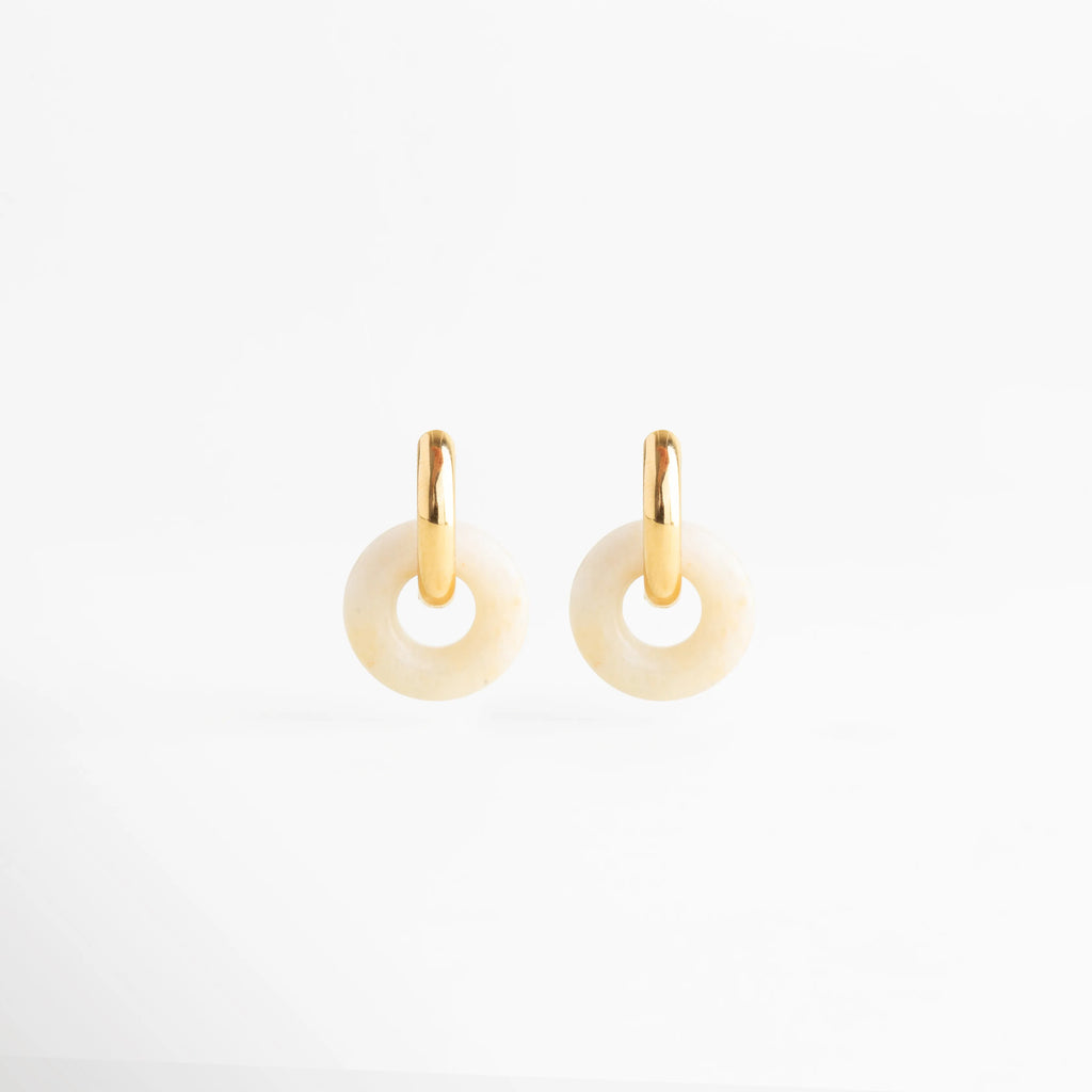 Aretes Emilia Hoops de acero inoxidable con baño de oro 18K y dije circular de ágata natural, Arracadas doradas minimalistas con piedra natural en forma de dona color crema sobre fondo blanco, Joyería de acero inoxidable: aretes tipo hoop con piedra natural orgánica y acabado brillante, Detalle de pendientes Emilia con herraje dorado liso y dije circular de piedra natural veteada, Pendientes contemporáneos con baño de oro de 18 quilates y detalles de ágata blanca.