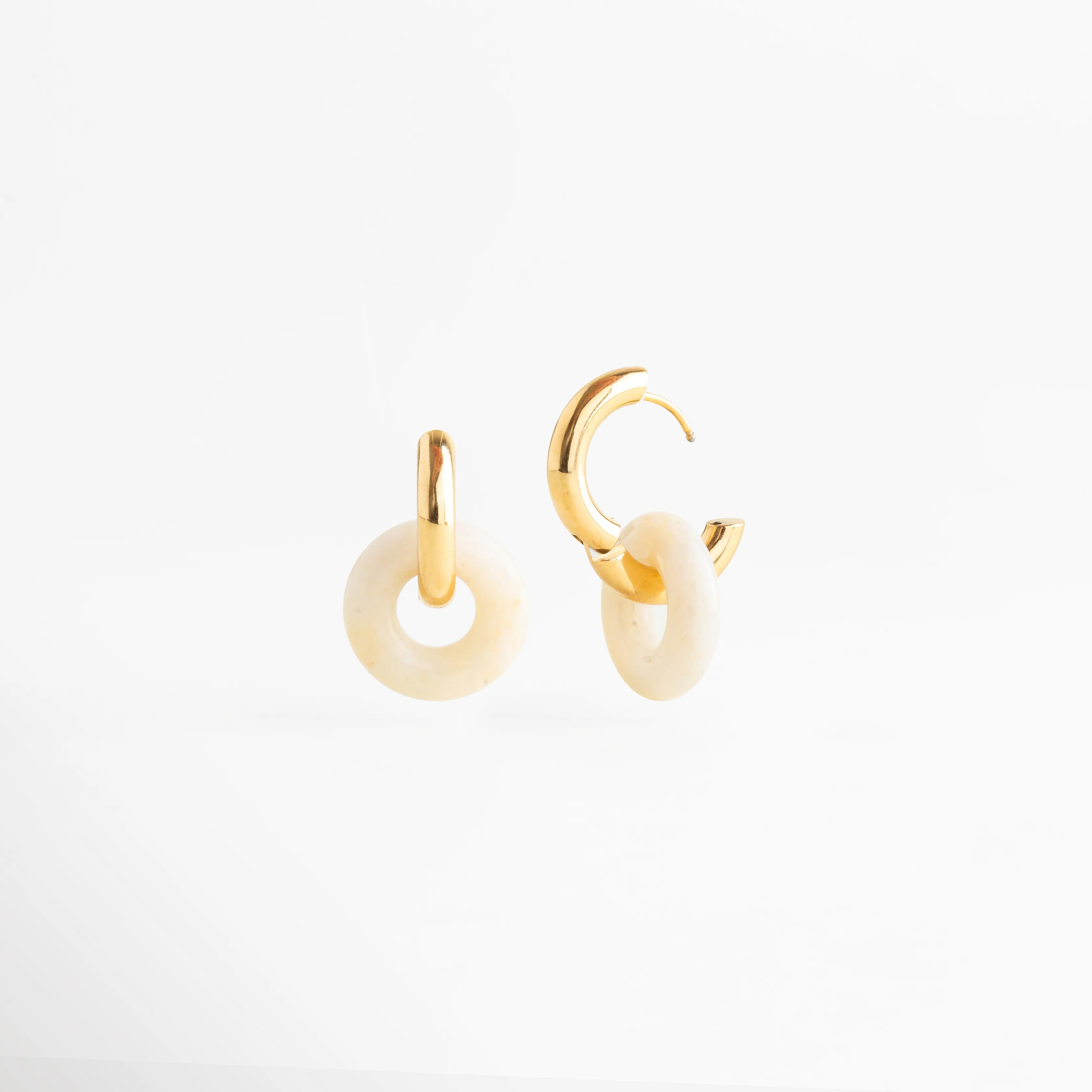 Vista lateral de los aretes Emilia Hoops mostrando el sistema de cierre de bisagra dorado, Pendientes de acero inoxidable con baño de oro abiertos para mostrar la funcionalidad del broche, Detalle del perfil del dije de piedra natural y el grosor del aro dorado de 0.4 cm, Perspectiva angular de las arracadas con piedra natural resaltando el acabado pulido espejo, Fotografía de producto mostrando el mecanismo de seguridad de los aretes dorados Emilia.