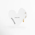 Set de tres aretes dorados de acero inoxidable con broquel solitario, arete curvo y mini arracada de zirconia, Trío de aretes dorados estilo constelación de Amalaya Jewelry en tarjeta blanca con forma de corazón, Joyería de acero inoxidable: arete trepador curvo con piedras brillantes y huggie de oro, Aretes resistentes al agua e hipoalergénicos para tres perforaciones de lóbulo, Detalle de ear stack dorado con zirconias y arete curvo sobre fondo blanco.