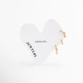Set de tres aretes huggies dorados de acero inoxidable con dijes de cruz, estrella y pedrería fina, Trío de mini arracadas chapadas en oro con amuletos de cruz y estrella de Amalaya Jewelry, Joyería de acero inoxidable: aretes de aro pequeños con dijes colgantes religiosos y celestiales, Aretes para tres perforaciones dorados hipoalergénicos y resistentes al agua sobre tarjeta blanca, Detalle de combinación para lóbulo con arracadas de oro y zirconias brillantes.