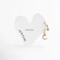 Dúo de mini arracadas doradas de acero inoxidable con dijes de luna y piedra azul turquesa, Dos aretes huggies de oro con zirconias colgantes celestiales de Amalaya Jewelry, Joyería de acero inoxidable: aretes de aro pequeños con dije de media luna turquesa y estrella, Aretes dorados con piedras de colores resistentes al agua sobre tarjeta blanca en forma de corazón, Detalle de ear stack de temática cósmica y mística con destellos turquesas en oro. 