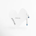 Dúo de aretes dorados en oro blanco de acero inoxidable con flor azul y barra colgante en degradado, Dos huggies plateados con zirconias de color azul y lavanda sobre tarjeta blanca de Amalaya Jewelry, Joyería de acero inoxidable hipoalergénica: mini arracadas con dijes colgantes de flores y piedras baguette, Aretes resistentes al agua color plata con piedras de colores para múltiples perforaciones, Detalle de combinación de aretes asimétricos con degradado púrpura y azul en oro blanco sobre fondo blanc
