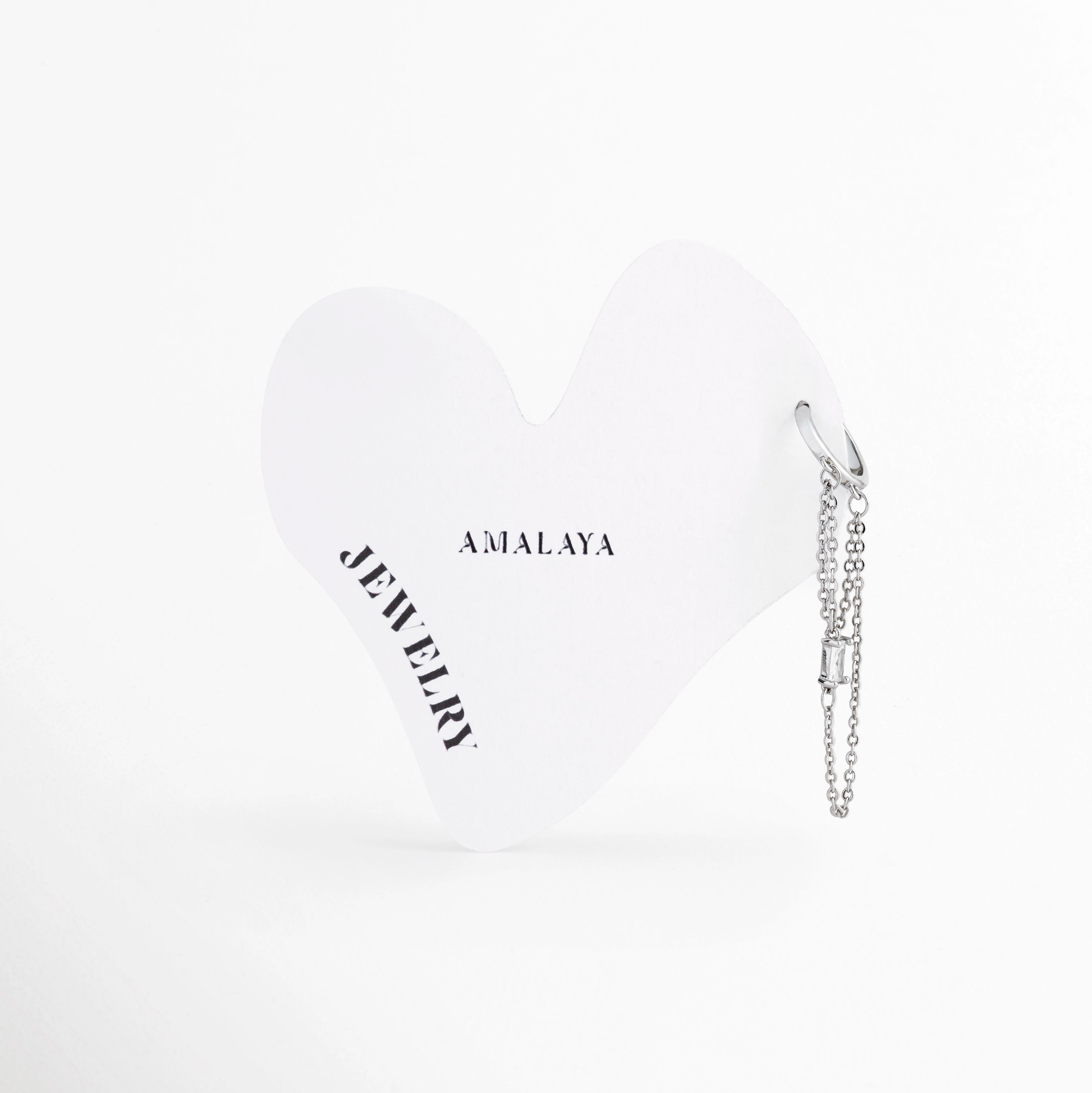 Piercing de cartílago tipo huggie plateado con doble cadena colgante y zirconia, Piercing de acero inoxidable para hélix con cadena fina sobre tarjeta de Amalaya Jewelry, Joyería para oreja: piercing plateado con caída de cadena y piedra corte baguette, Piercing hipoalergénico de oro blanco con detalle de zirconia rectangular brillante, Primer plano de piercing de aro con cadena drapeada para hélix o conch.